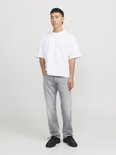 Man met korte, zwarte mullet, draagt een witte oversized top en lichtgrijze jeans. Zwarte schoenen, hele figuur.