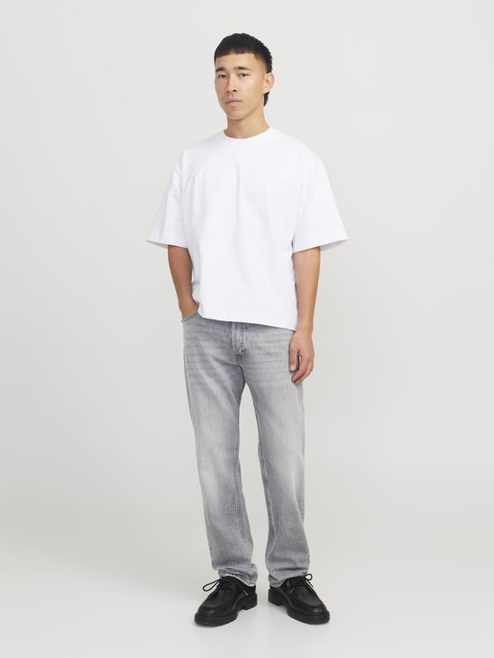 Man met korte, zwarte mullet, draagt een witte oversized top en lichtgrijze jeans. Zwarte schoenen, hele figuur.