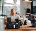 Donkergrijs Jackery Explorer 500 powerstation met oranje accenten, op een houten tafel, met camera-apparatuur.