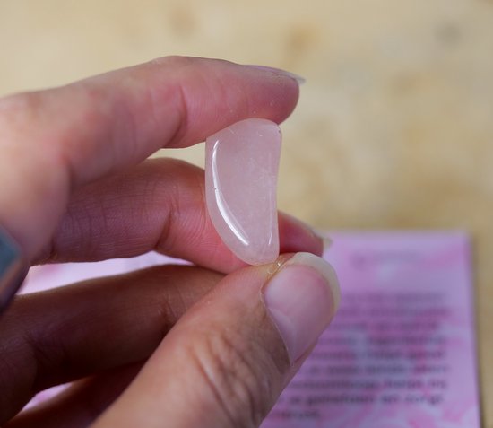 Een hand houdt een gladde, lichtroze rozenkwarts edelsteen vast. De steen is ovaal met een platte kant.