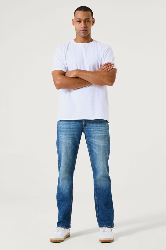 Man in een witte T-shirt en loszittende blauwe spijkerbroek met lichte vervaging.