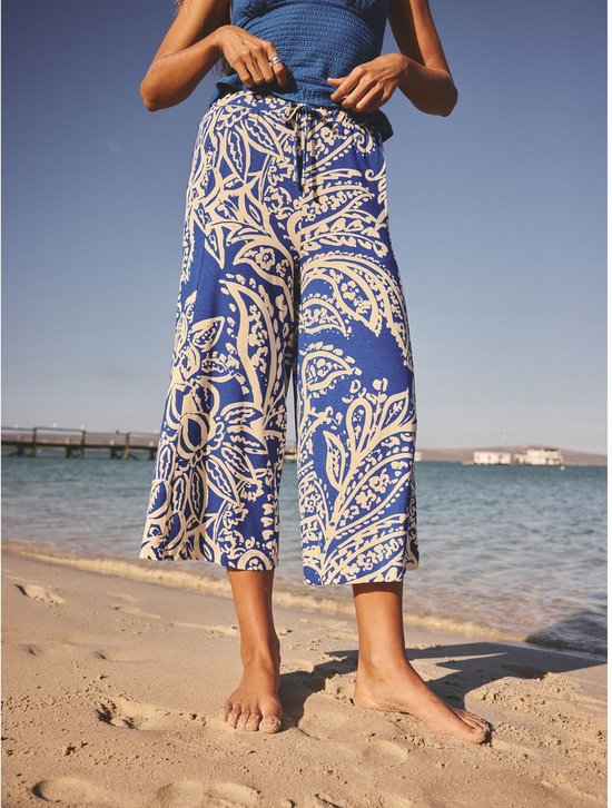 Zicht op de voorkant van een vrouw die een culotte met blauwe en crème paisley print draagt, op het strand.