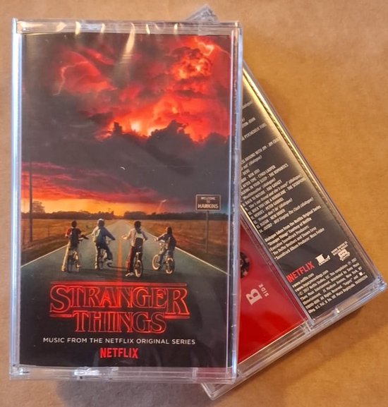 Twee cassettebanden. Eén met 'STRANGER THINGS' artwork van vier kinderen op fietsen onder een zonsondergang. Een andere rode band met tracklist.