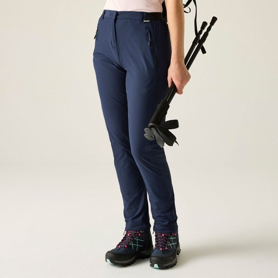 Zijkant van een donkerblauwe, aansluitende wandelbroek gedragen door een model, met wandelstokken en schoenen.