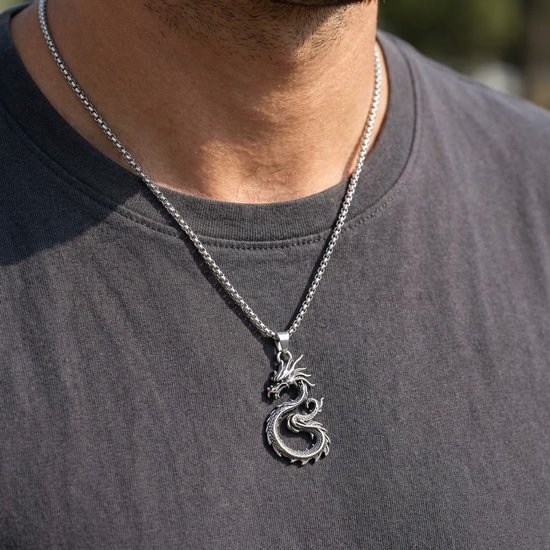 Zilverkleurige ketting met gedetailleerde drakenhanger om de nek van een man.