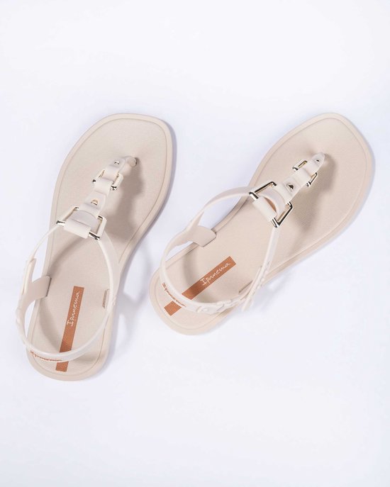 Paar lichtbeige Ipanema slippers, van bovenaf gezien, met enkelbandjes en banden over de wreef met gouden gespen.