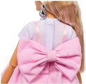 Barbiepop met grote roze strik op de rug van de jurk, een witte top en sprankelende oorbellen.