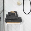 Stapel donkergrijze handdoeken met een houten borstel bovenop, in een badkamer.