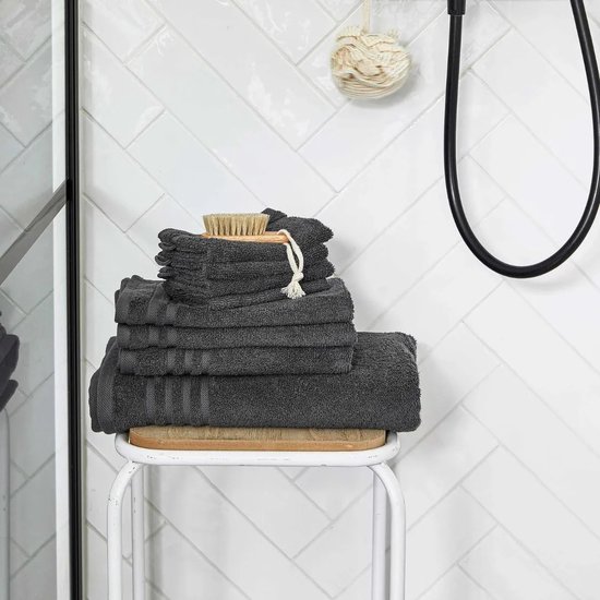Stapel donkergrijze handdoeken met een houten borstel bovenop, in een badkamer.