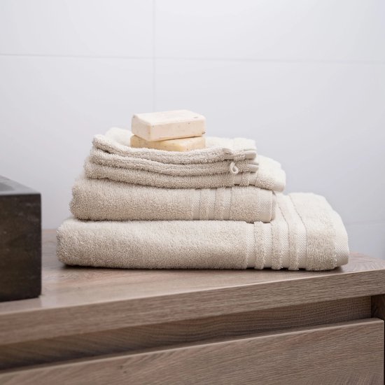 Une pile de serviettes beiges avec deux savons sur le dessus, sur un meuble en bois.