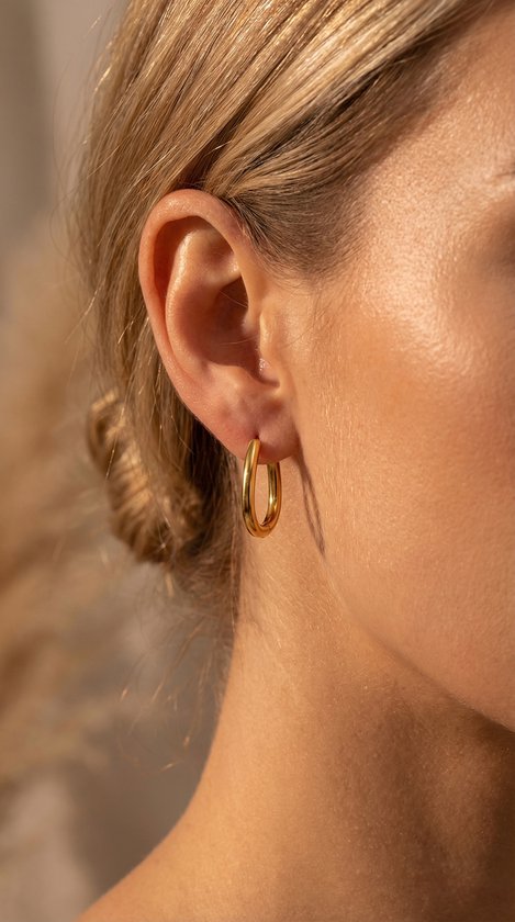 Gouden, ovale oorringen met een dubbele buis, gedragen door een model.