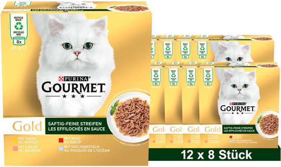 Doos met Gourmet Gold kattenvoer en meerdere gestapelde dozen. Een witte kat met groene ogen kijkt naar de kijker. De doos toont informatie over de smaken: kip, rund, zalm, vis.