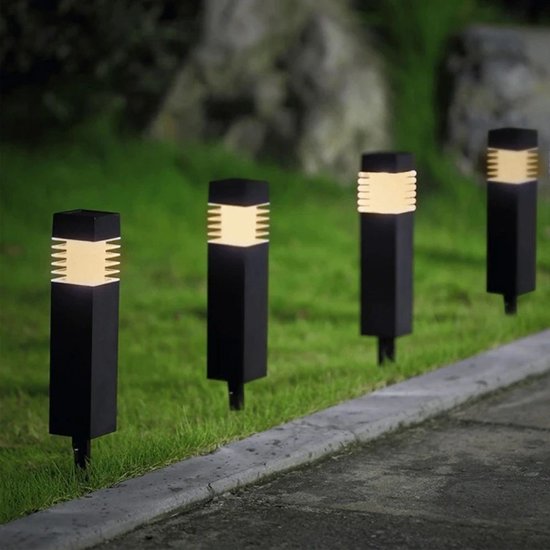 Rij van vier zwarte, vierkante tuinlampen met warm wit licht, geplaatst langs een gazon en stoep.