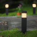 Een zwarte, vierkante tuinlamp met geribd glazen kap en warm wit licht, geplaatst in gras.