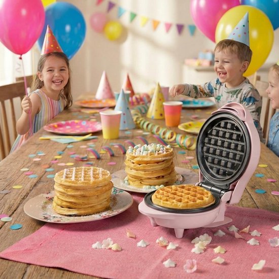 Roze mini wafelijzer op een feesttafel met kinderen, wafels, ballonnen en slingers.