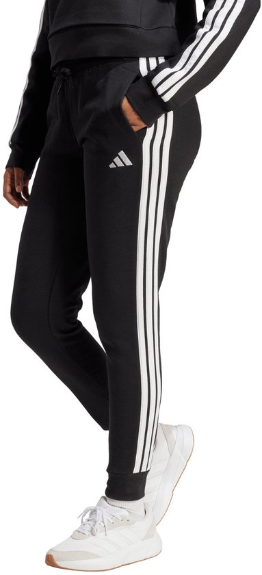 Zwarte joggingbroek met witte Adidas strepen op de zijkant, gedragen met witte sneakers.
