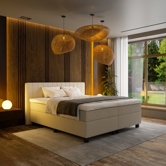Un boxspring beige avec une tête de lit rayée, du linge de lit blanc, une couverture grise et trois suspensions en rotin.