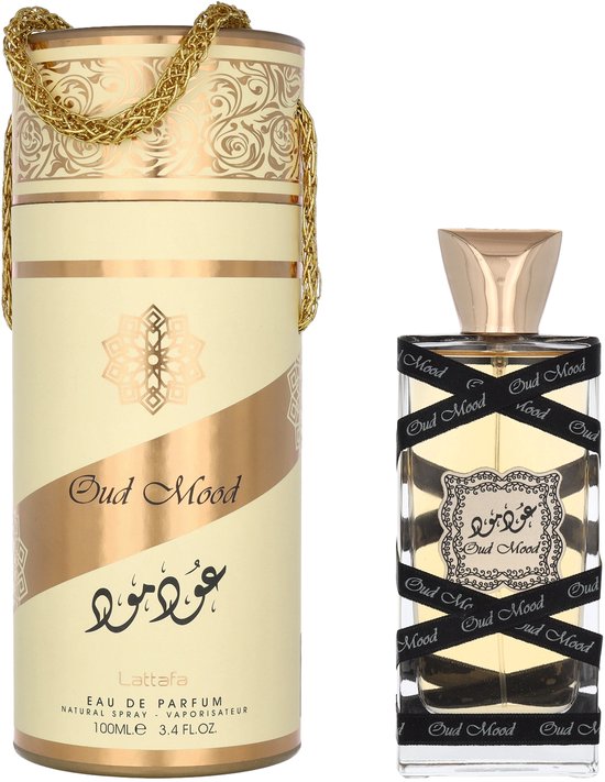 Oud Mood parfumfles met gouden dop, omwikkeld met zwart lint met "Oud Mood" erop. Bijpassende cilinderverpakking met gouden opdruk.
