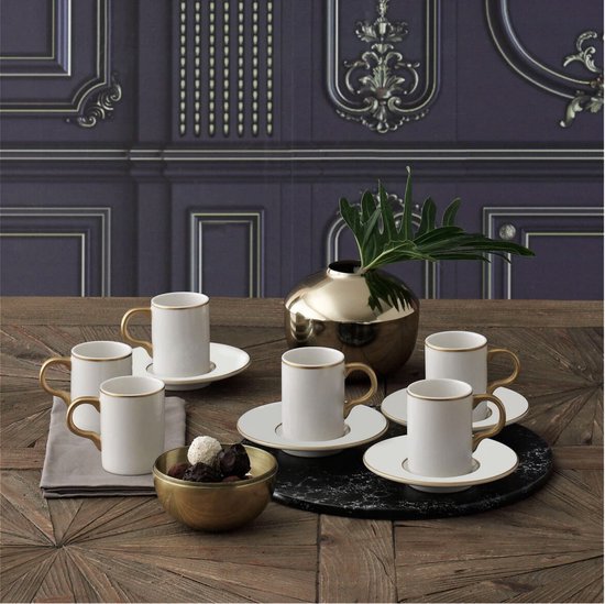 Set van zes witte, slanke koffiekopjes met gouden randen en handvatten op bijpassende schoteltjes, naast een gouden vaas en een schaal met chocolade.