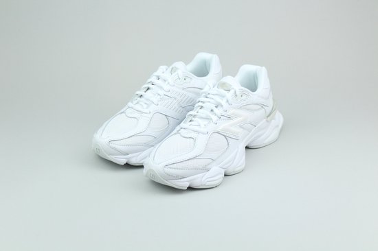 Paar witte New Balance 9060 sneakers op een grijze achtergrond.