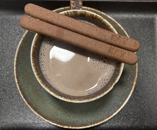 Tasse de chocolat chaud, garnie de deux cuillères à café comestibles au chocolat avec le mot EAT.