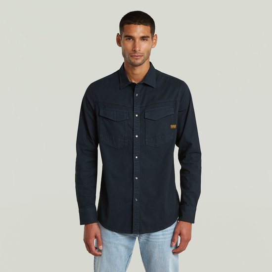 Model draagt een donkerblauw G-Star overhemd met twee borstzakken en lichtblauwe jeans.