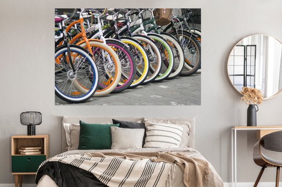 Une rangée de vélos colorés avec des jantes orange, bleues, blanches, roses et jaunes, au-dessus d'un lit dans une chambre.