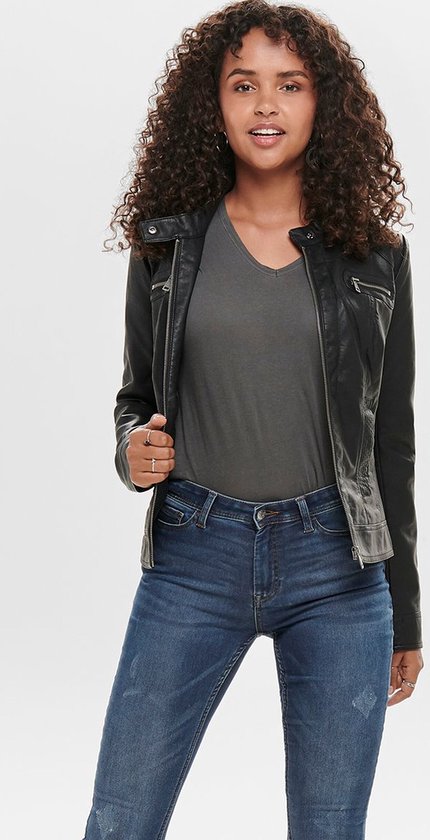 Model met krullend haar draagt zwart kunstleren jack met grijze top en jeans.