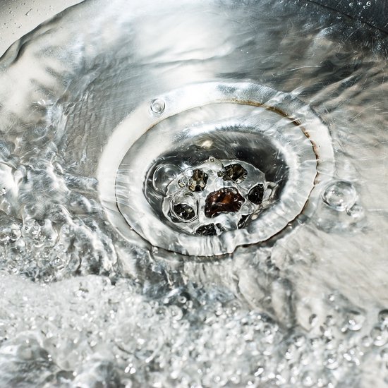 Water stroomt door een gootsteenafvoer met luchtbellen.
