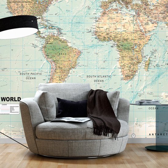 Gedetailleerde wereldkaart achter een comfortabele grijze fauteuil met een zwart kussen en bruine plaid.