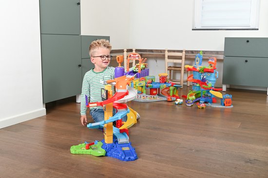 Jongen met bril en gestreept shirt speelt met kleurrijke racebaan in woonkamer.