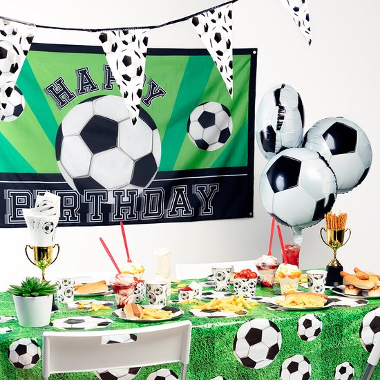 Gedekte tafel met groene tafelkleed met voetbalprint, ballonnen, banner en eten.