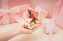 Miniatuur badkamer met rode dak, douchegordijn en roze badkuip vastgehouden in hand tussen roze cadeaus.
