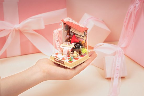 Miniatuur badkamer met rode dak, douchegordijn en roze badkuip vastgehouden in hand tussen roze cadeaus.