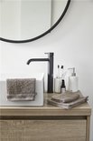 Gants de toilette taupe sur un meuble de salle de bain en bois avec un robinet noir et un miroir.