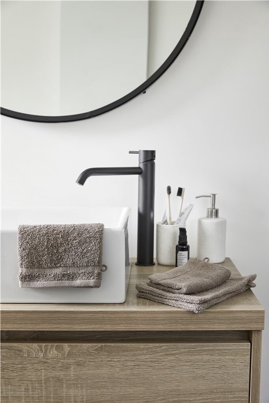 Gants de toilette taupe sur un meuble de salle de bain en bois avec un robinet noir et un miroir.