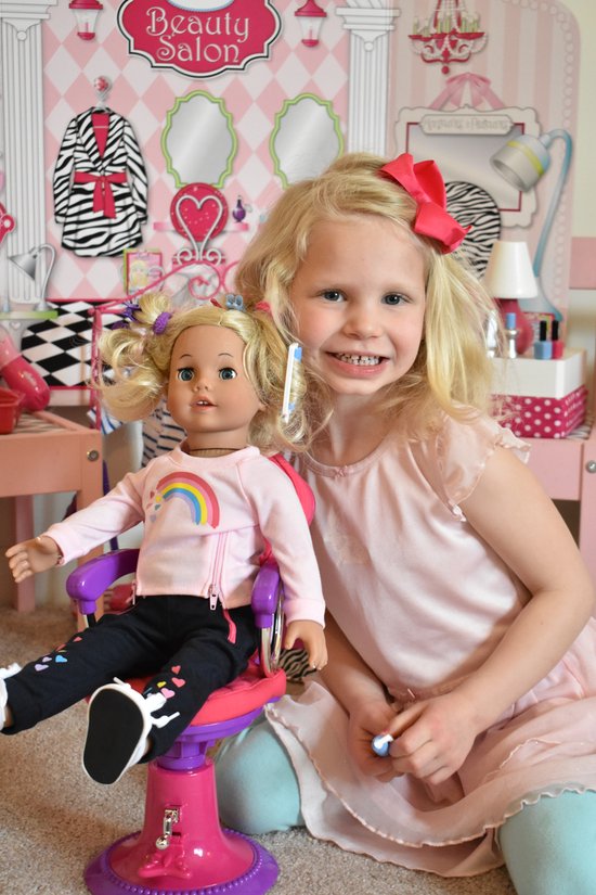 Een meisje met blond haar en een rode strik in haar haar speelt met een pop met blond haar in een roze jurkje.