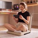 Vrouw met koptelefoon zit op beige vloerstoel, speelt op Nintendo Switch.