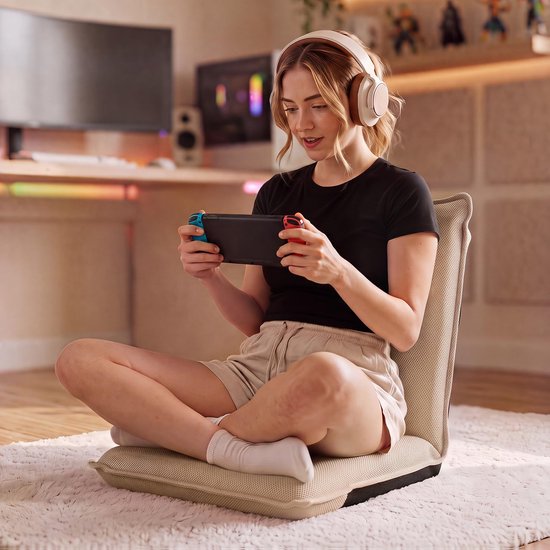 Vrouw met koptelefoon zit op beige vloerstoel, speelt op Nintendo Switch.