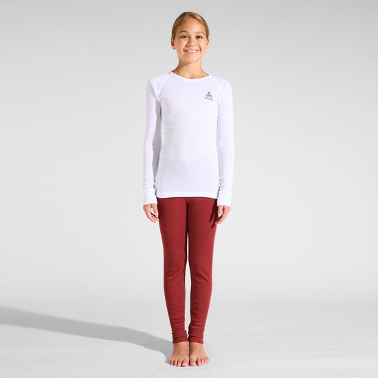 Staand meisje in een wit Odlo thermoshirt met lange mouwen en rode legging op blote voeten.