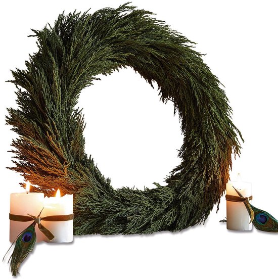 Groene kerstkrans van dennentakken met twee brandende witte kaarsen versierd met pauwenveren.