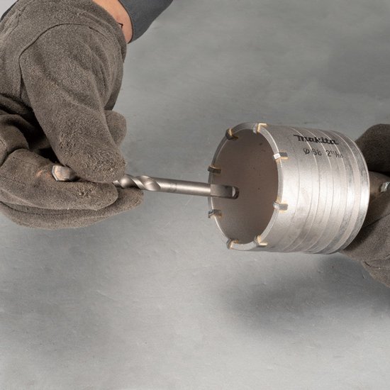 Handen in grijze werkhandschoenen plaatsen een boor in een Makita-gatzaag van 68 mm.