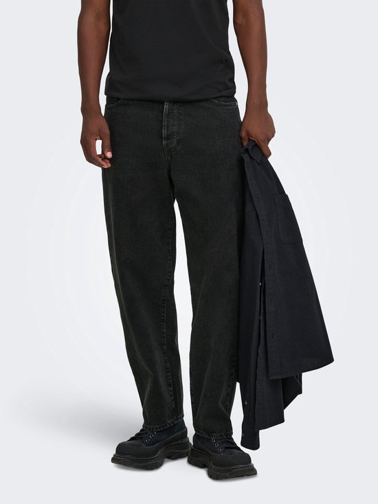 Close-up van de pasvorm van een zwarte jeans bij een model dat een zwarte jas vasthoudt.