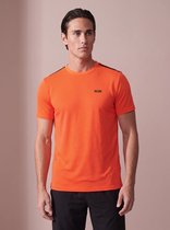 Model in oranje sportshirt met horizontale strepen, zwart SJS-logo en zwarte broek.
