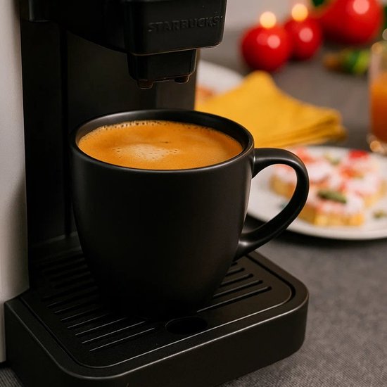 Zwarte Studio Tavola koffiekop gevuld met verse koffie onder een Starbucks koffiezetapparaat.