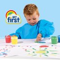 Een jongen in een blauw schort met zijn vinger in blauwe verf, op een papier met tekeningen.