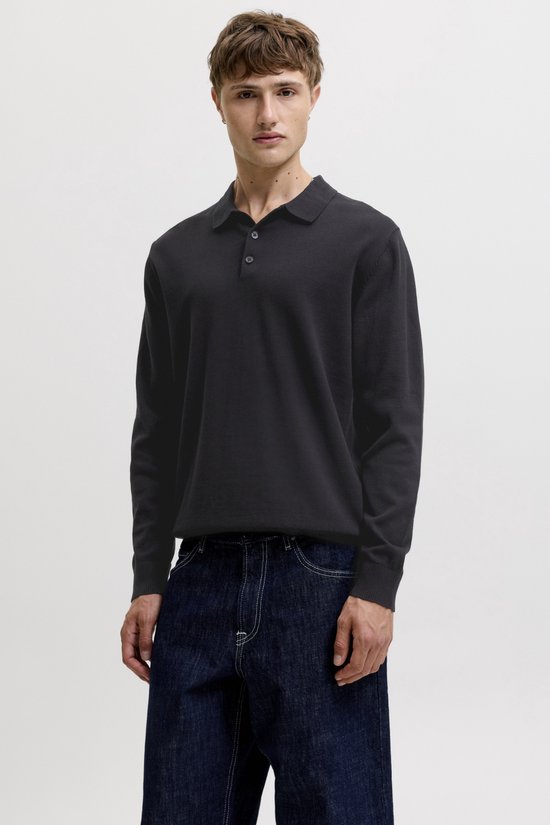Model draagt een zwart longsleeve poloshirt met knoopjes en donkere, wijde jeans.