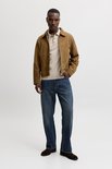 Man met beige polo, bruine jas en spijkerbroek.