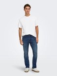 Model draagt een wit T-shirt en een regular fit blauwe jeans, gecombineerd met sneakers in wit en beige.