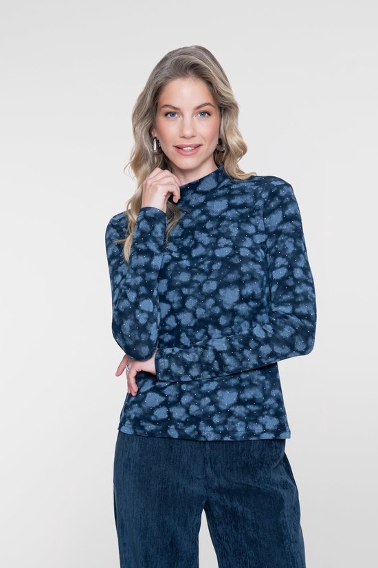 Model draagt een donkerblauwe top met lange mouwen en hoge hals met vlekkenprint en witte spikkels, gecombineerd met een effen donkerblauwe broek.